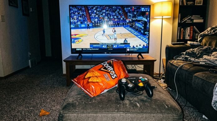 Center is my actual TV (55-inch TCL, nothing fancy) paused mid-play on a college basketball game, screen glare catching the room lights